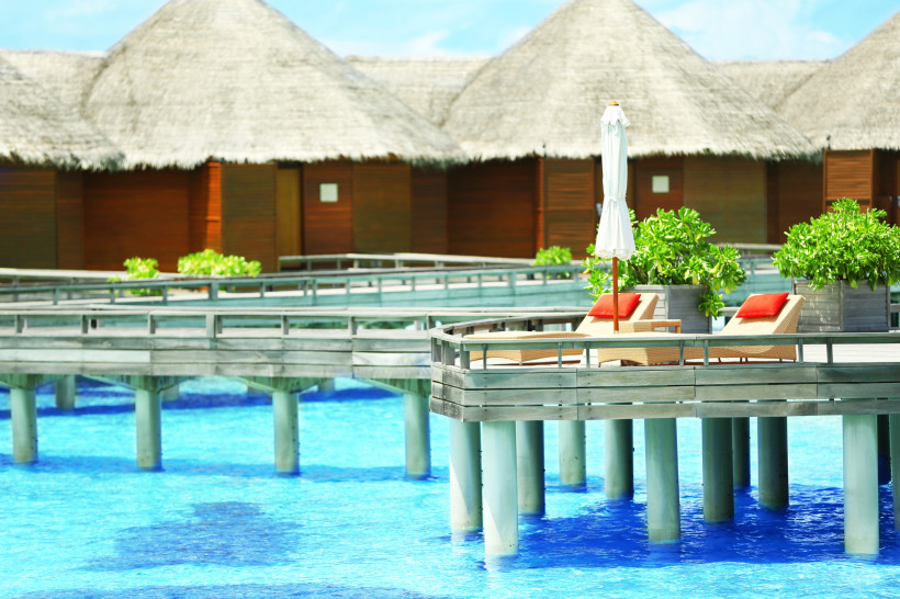 Malediven -  Baros Maldives Luxuriöse Wasserbungalows auf den Malediven mit Holzstegen über dem türkisblauen Meer und Sonnenterrassen mit Liegen.