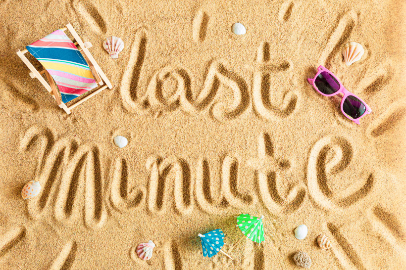 Sommerliches Strandmotiv mit dem Schriftzug 'last minute' im Sand, Liegestuhl, Sonnenbrille, Muscheln und Cocktail-Schirmchen