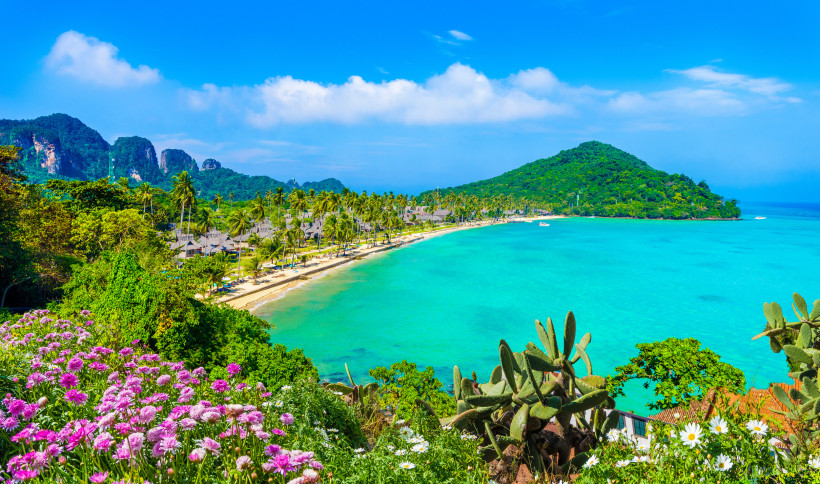Krabi Strandblick – Tropische Küste mit türkisblauem Wasser Panoramablick auf einen Strand in Krabi mit türkisblauem Meer, üppiger Vegetation, Palmen und farbenfrohen Blumen – ideal für einen Thailand Strandurlaub.