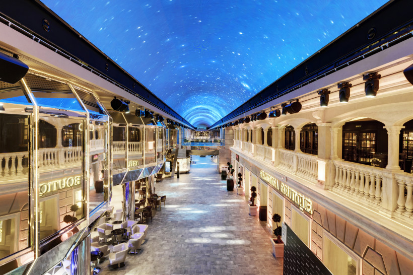 MSC Grandiosa: Öffentlicher Bereich Promenade Galleria Grandiosa mit LED-Dome Promenade der MSC Grandiosa mit Galleria Grandiosa und blau beleuchteter LED-Kuppeldecke, flankiert von Geschäften und Sitzbereichen