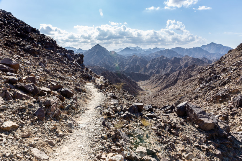 Wanderpfad durch die felsige Berglandschaft des Wadi Shawka in Ras Al Khaimah mit Aussicht auf Gipfelketten.
