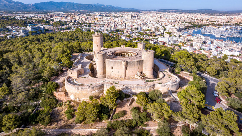 Luftaufnahme des Castell de Bellver, runde Burganlage oberhalb von Palma de Mallorca, umgeben von Pinienwald und Stadtpanorama