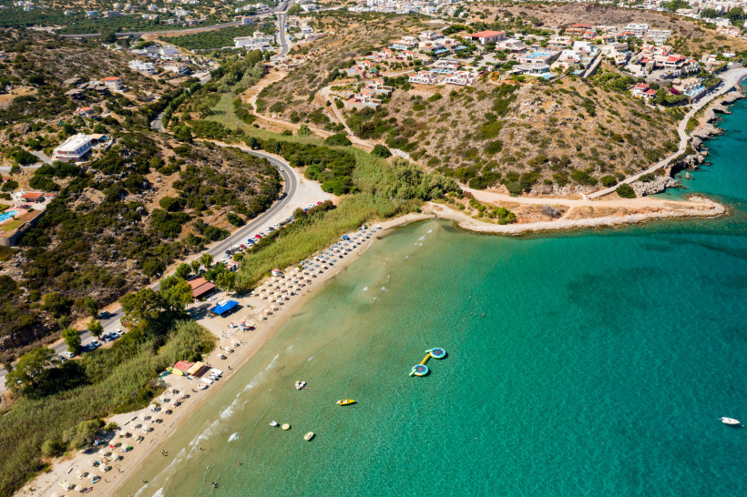 Luftaufnahme vom Almyros Beach bei Agios Nikolaos mit Sandstrand, Sonnenschirmen und türkisfarbenem Meer