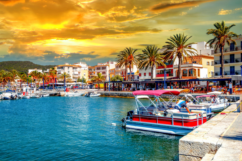 Hafenpromenade von Port d’Andratx mit Booten, Palmen und Gebäuden bei Sonnenuntergang