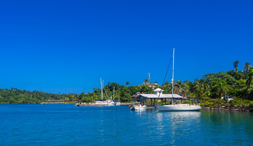 Tropischer Hafen mit Segelbooten – Paradiesisches Reiseziel am Meer Tropischer Yachthafen mit Segelbooten, türkisblauem Wasser und üppig grüner Landschaft unter strahlend blauem Himmel.