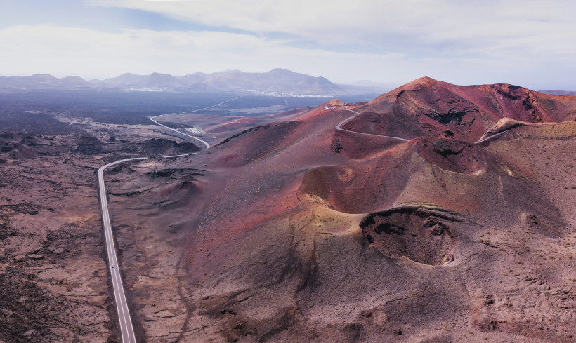 Lanzarote aus der Vogelperspektive – spektakuläre Kraterlandschaft im Timanfaya-Nationalpark Luftaufnahme der roten Vulkanlandschaft mit Kratern und kurvigen Straßen im Nationalpark Timanfaya auf Lanzarote