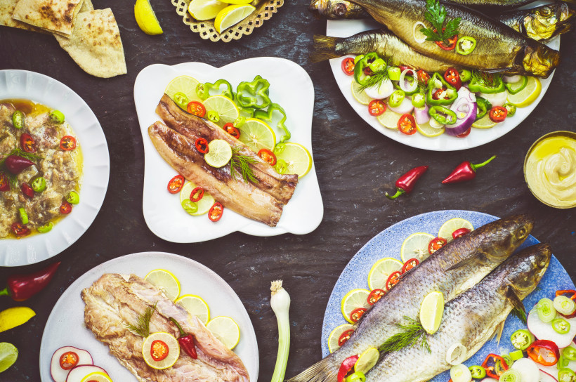 Ägypten - Sharm el Sheikh Verschiedene orientalische Fischgerichte auf bunten Tellern, dekoriert mit Zitronen-, Chili- und Zwiebelscheiben sowie frischen Kräutern. Zu sehen sind ganze Fische, Filets und mariniertes Fischfleisch, begleitet von Fladenbrot, eingelegtem Gemüse, Senf u