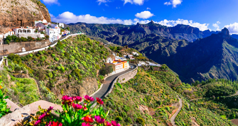 Bergdorf mit weißen Häusern und bunten Fassaden am steilen Hang von Gran Canaria, umgeben von grünen Terrassen und Schluchten.