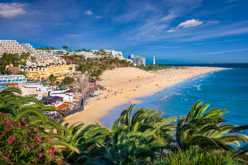 Strand von Morro Jable auf Fuerteventura mit Promenade, Hotels, Palmen und dem weißen Leuchtturm im Hintergrund