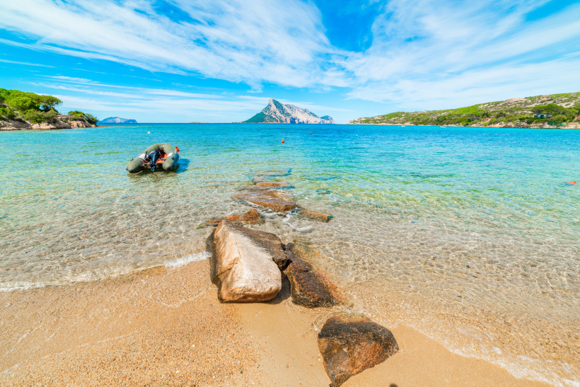 Strand auf Sardinien mit klarem Wasser, Felsen im Sand und Blick auf die Insel Tavolara – beliebtes Reiseziel für Badeurlaub und Naturfreunde