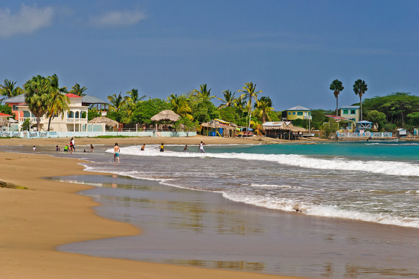Karibikstrand mit Palmen und Badegästen – tropisches Urlaubsparadies am Meer Karibischer Sandstrand mit türkisblauem Meer, Palmen und kleinen Strandhäusern – Badegäste genießen die Sonne und das warme Wasser.