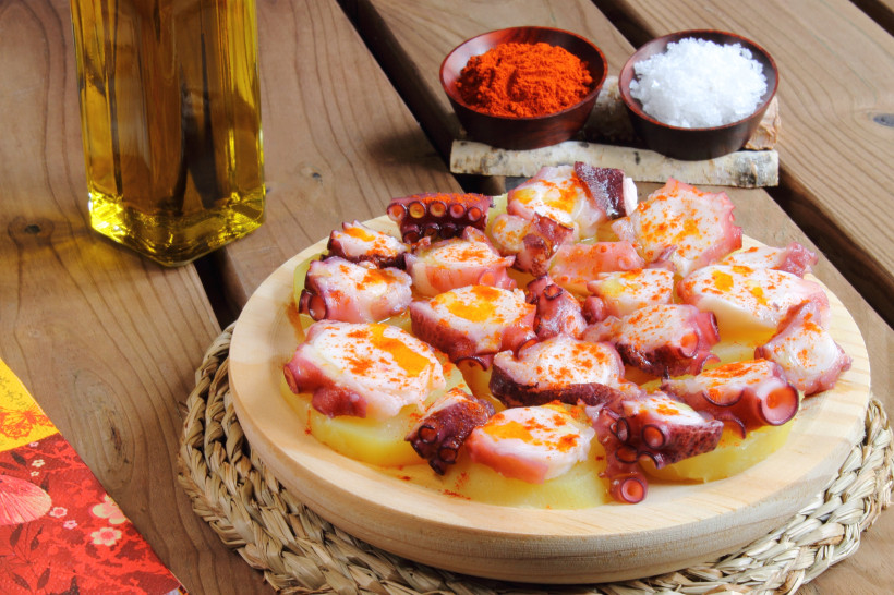 Pulpo a la Gallega: Oktopusstücke auf Kartoffelscheiben mit Olivenöl und Paprikapulver auf Holzbrett