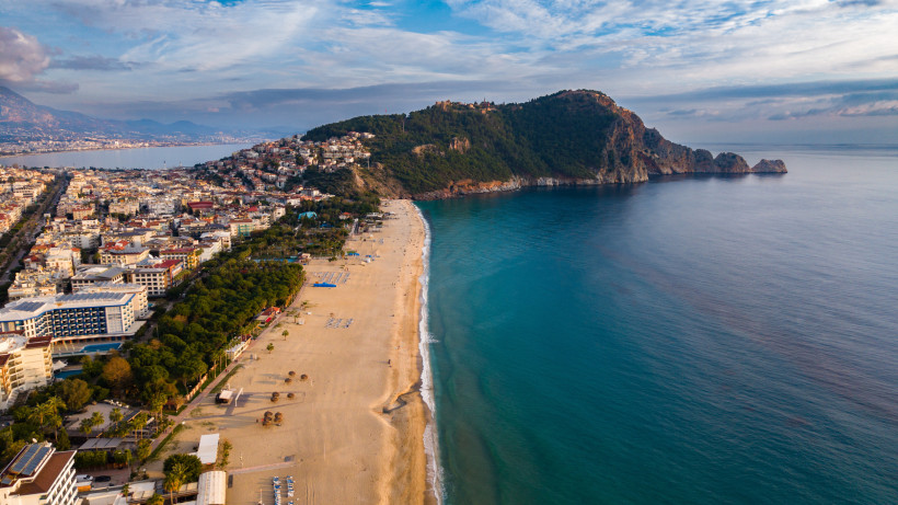 Drohnenaufnahme vom Kleopatra-Strand in Alanya mit Blick auf die Stadt, das Meer und den imposanten Burgfelsen