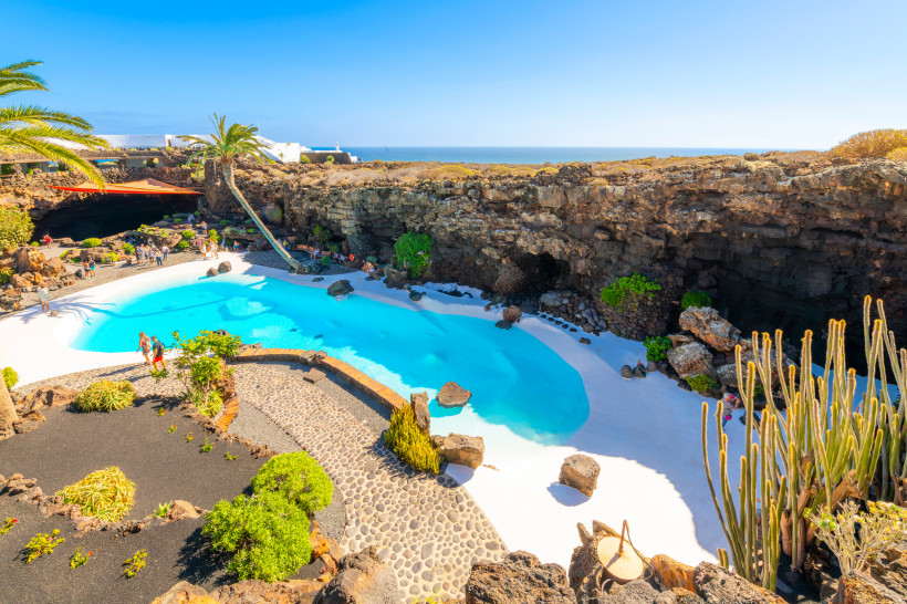 Schwimmbecken in einer Lavahöhle bei Jameos del Agua auf Lanzarote, mit Palmen, Vulkanfelsen und Blick auf den Atlantik