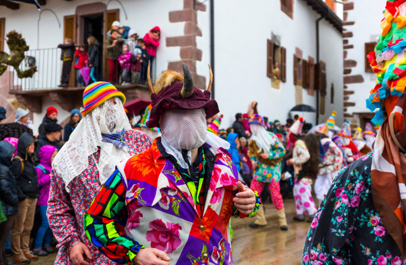Spanien Menschen in auffälligen, bunt gemusterten Kostümen und verschleierten oder mit Hörnern verzierten Masken nehmen an einem Karnevalsumzug teil. Die Straße ist von Zuschauern gesäumt, viele stehen in warmer Kleidung auf Balkonen oder an den Hauswänden. Die V