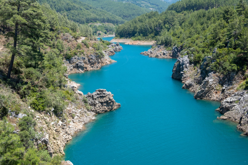 Der Dimçay-Fluss in Alanya fließt durch eine felsige Landschaft mit klarem Wasser, umgeben von dichtem Pinienwald und natürlichen Uferbereichen.