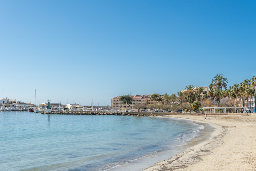 Bucht von Platja d’es Port mit Sandstrand, ruhigem Wasser und Yachthafen im Hintergrund