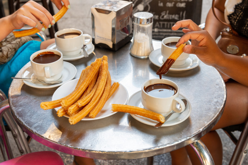 Churros auf einem Teller mit Tassen heißer Schokolade auf einem Cafétisch