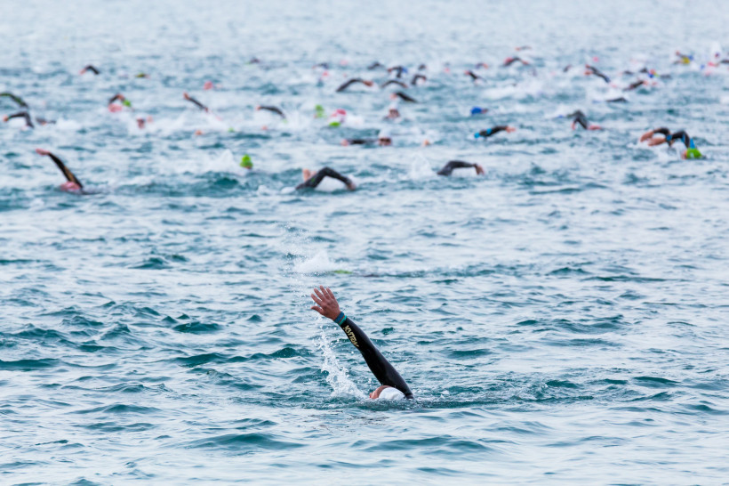 Lanzarote Gruppe von Schwimmern in Neoprenanzügen nimmt an einem Freiwasser-Wettbewerb im offenen Meer teil. Eine Person im Vordergrund hebt den Arm beim Kraulschwimmen.