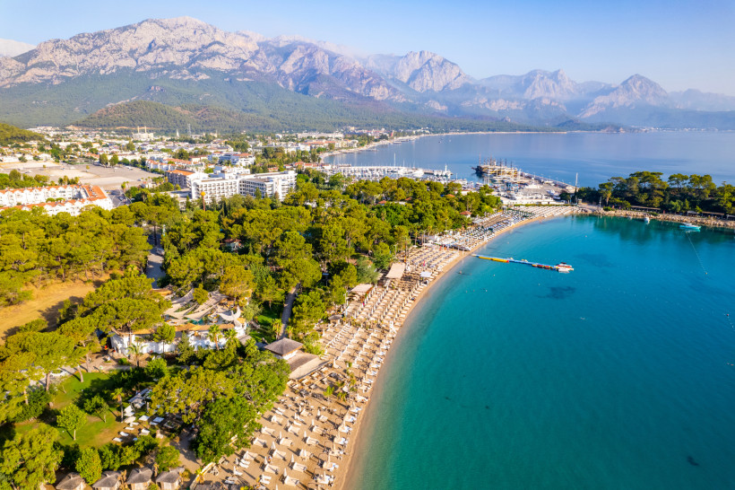Kemer Strand an der Türkischen Riviera – Pinienwälder, türkisblaues Meer und Taurusgebirge Luftaufnahme von Kemer an der Türkischen Riviera mit Pinienwäldern, breitem Strand, türkisblauem Meer, Marina und dem imposanten Taurusgebirge im Hintergrund.