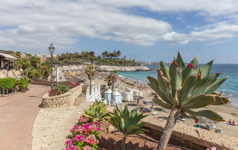 Playa del Duque: Strandabschnitt mit Promenade, Felsen und türkisblauem Meer Blick auf die Playa del Duque mit Strand, Sonnenschirmen, Promenade und Küste am Atlantik