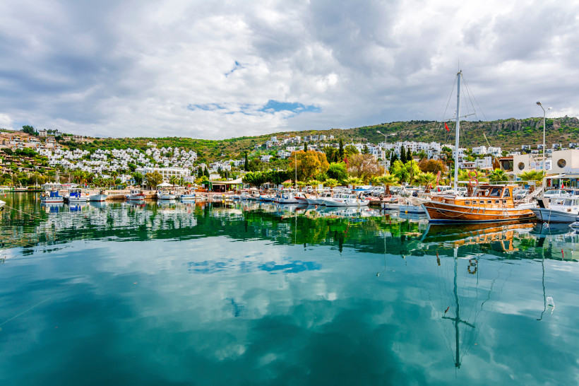 Hafen mit Segel- und Ausflugsbooten, Spiegelungen im Wasser und weißer Küstenort im Hintergrund
