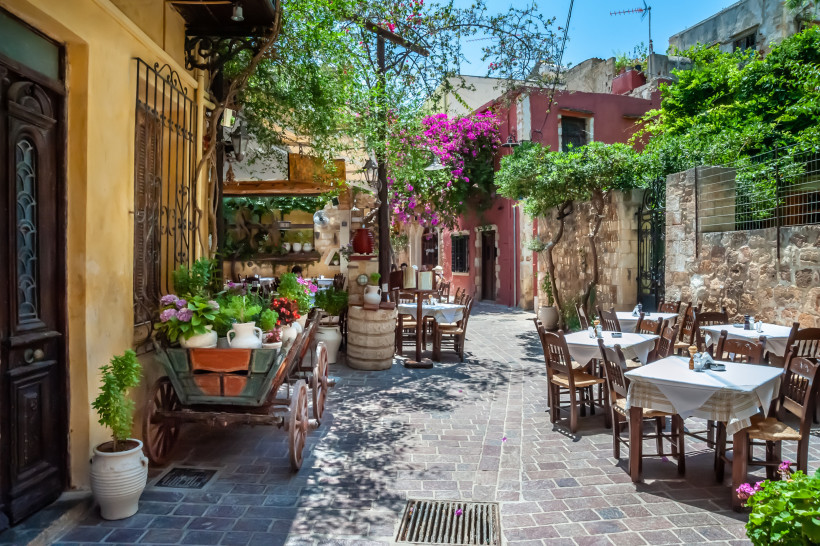 Außenbereich einer typischen Taverne in der Altstadt nahe Platanias mit gedeckten Tischen in einer schmalen Gasse