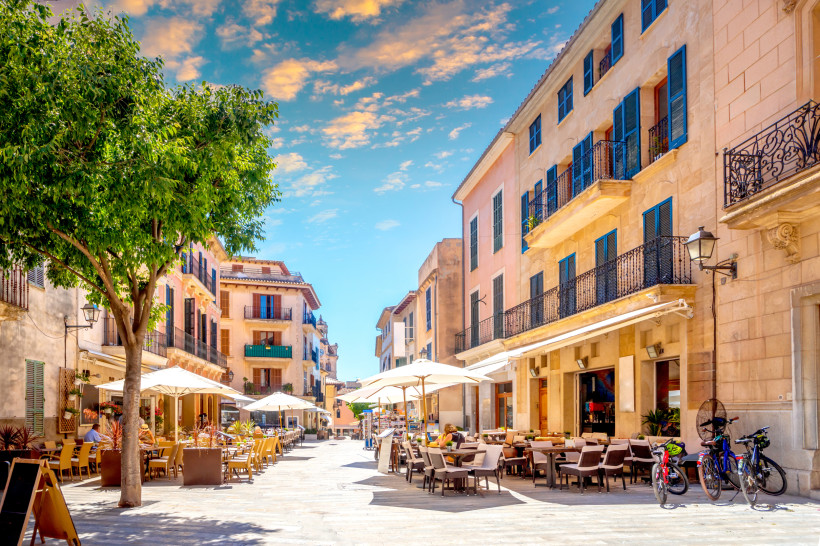 Straßencafé in der Altstadt von Alcúdia mit Sonnenschirmen, historischen Fassaden und blauem Himmel