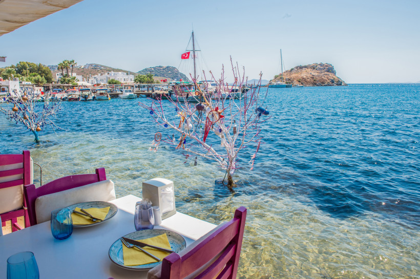 Restaurantterrasse direkt am Meer mit gedecktem Tisch und Blick auf Boote und Küste