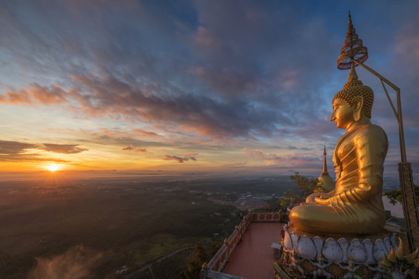 Tiger Cave Temple in Krabi, Thailand: goldene Buddha-Statue bei Sonnenaufgang mit weitem Blick über die Landschaft.
