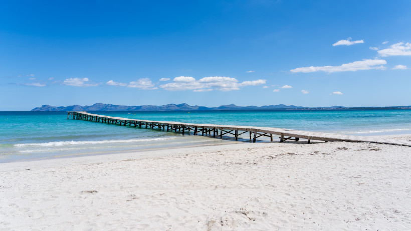 Playa de Muro, Mallorca Holzsteg am weißen Sandstrand von Playa de Muro auf Mallorca mit türkisfarbenem Wasser und Panoramablick auf die Bucht von Alcúdia