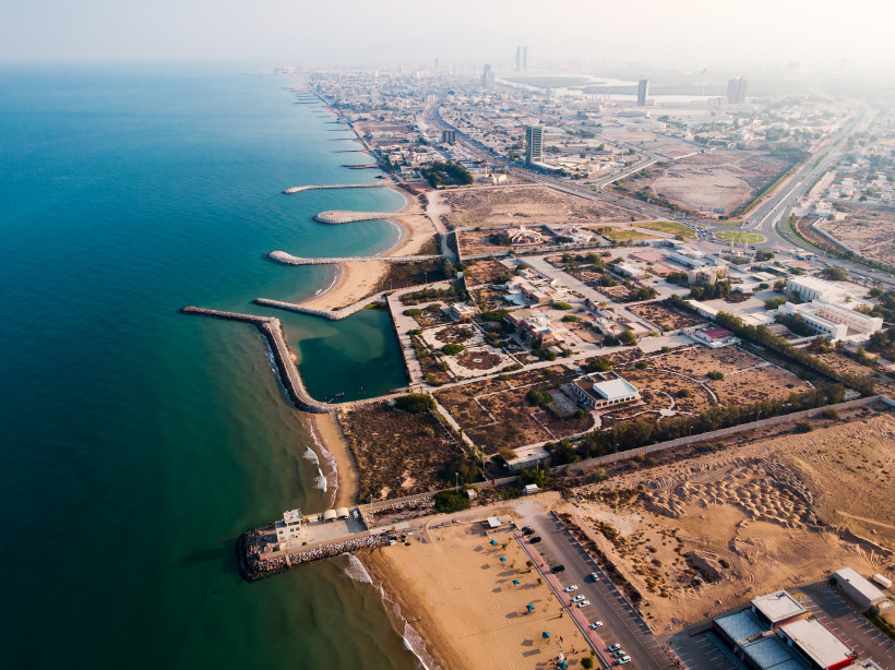 Luftaufnahme der Küste von Ras Al Khaimah mit Sandstrand, Meer und Wellenbrechern.
