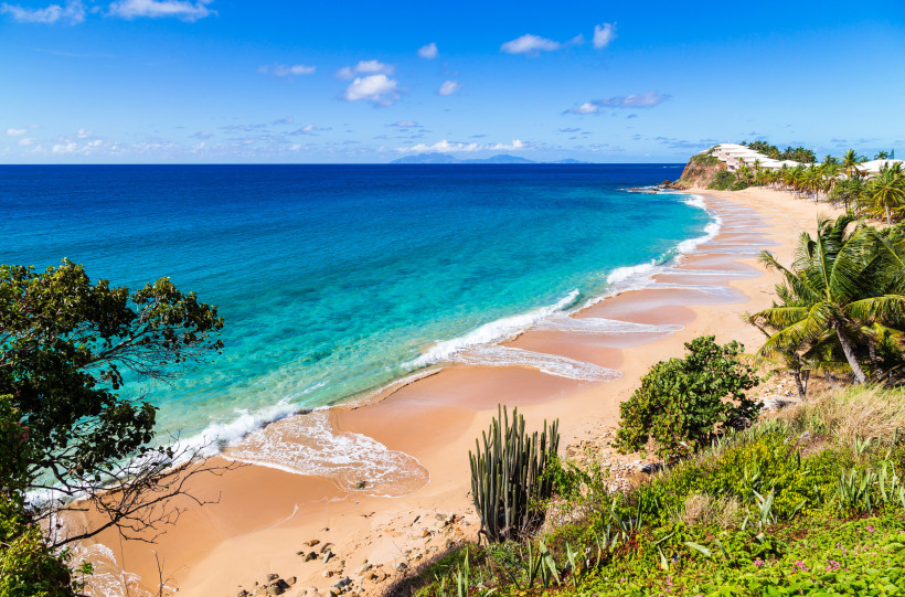 Küstenstrand auf Antigua mit türkisblauem Meer, hellem Sand und Palmen am Ufer