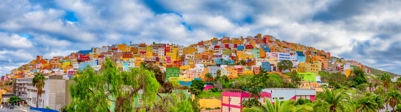 Panorama von Las Palmas de Gran Canaria mit dicht aneinandergebauten bunten Häusern am Hang unter wolkigem Himmel.