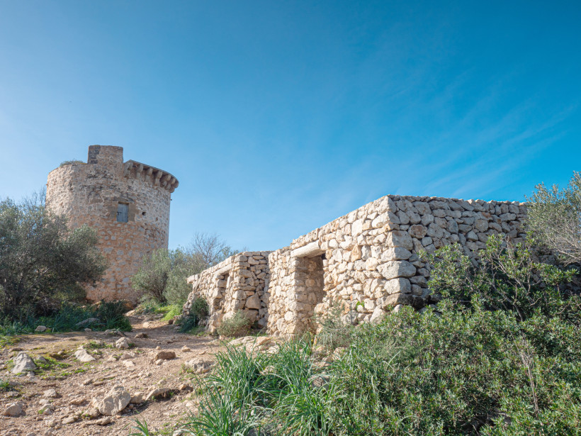 Torre de Cap Andritxol, runder steinerner Wachturm mit angrenzender Trockensteinmauer in mediterraner Vegetation