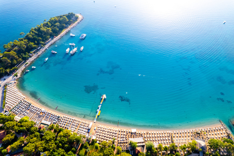 Luftaufnahme vom Moonlight Beach in Kemer mit halbmondförmigem Strand, Liegen, Booten und türkisblauem Meer