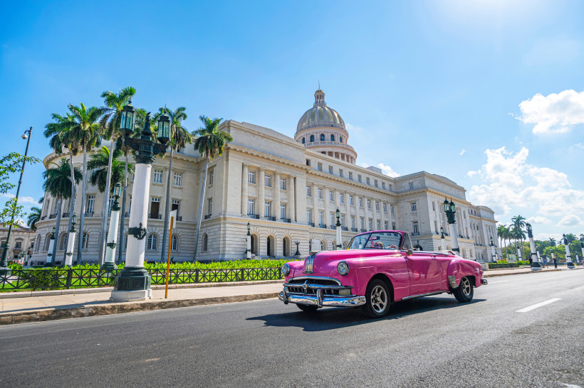 Pinker Oldtimer vor dem Capitolio Nacional in Havanna Kuba bei Sonnenschein mit Palmen im Hintergrund