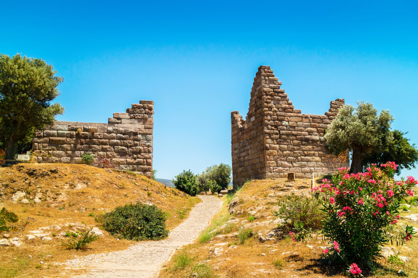 Antike Steinmauern und Stadttor von Halikarnassos bei Bodrum mit Fußweg, Bäumen und blauem Himmel
