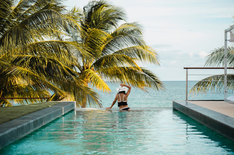Luxusferien in Mexiko Infinity-Pool mit einer Frau in einem weißen Hut, die auf das Meer blickt, umgeben von Palmen und tropischer Vegetation