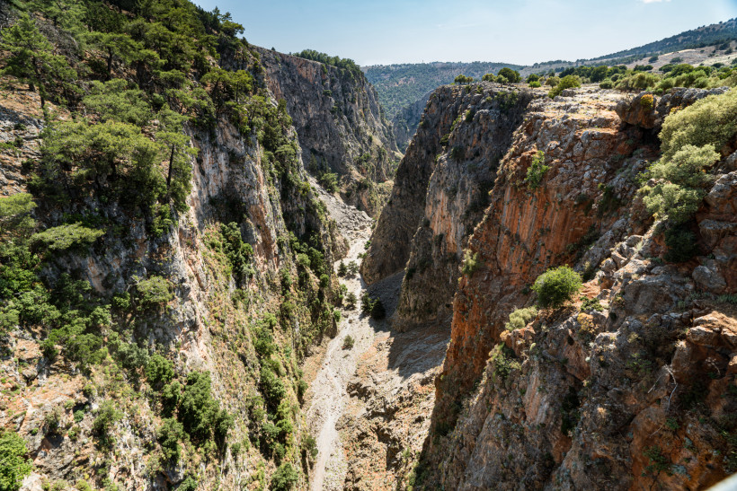 Tiefe Schlucht auf Kreta mit steilen Felswänden, grün bewachsenen Hängen und trockenem Flussbett in der Mitte