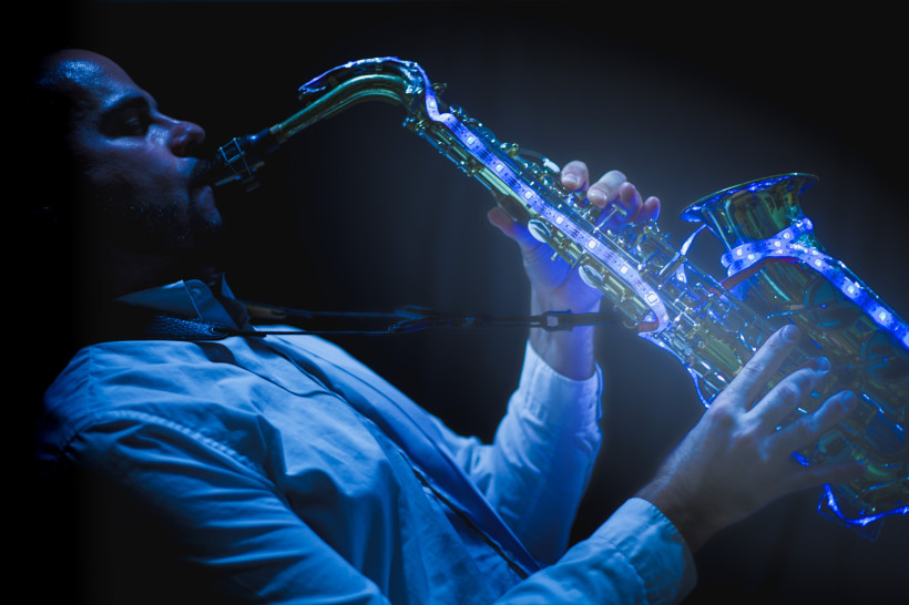 Ibiza Ein Musiker spielt Saxophon im Dunkeln. Das Instrument ist mit blauen LED-Lichtern beleuchtet. Der Mann trägt ein helles Hemd und ist konzentriert auf sein Spiel. Die Szene wirkt stilvoll und stimmungsvoll.