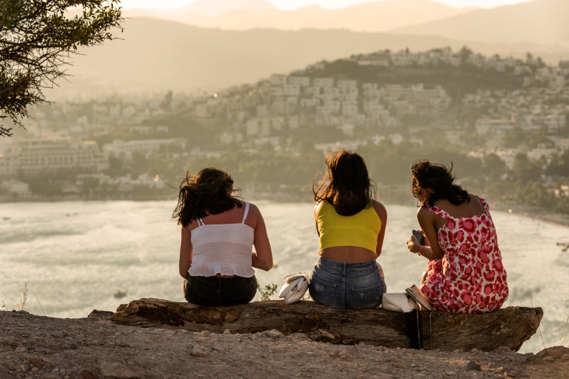 Drei Frauen sitzen an einem Aussichtspunkt über einer Küstenstadt in der Türkei mit Blick auf Meer, Bucht und Hügel im warmen Abendlicht