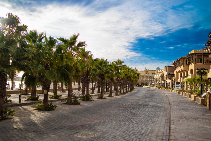 Sonnige Palmenpromenade in einem ägyptischen Ferienort Palmen gesäumte Promenade mit mediterranen Gebäuden und blauem Himmel in einem ägyptischen Badeort.