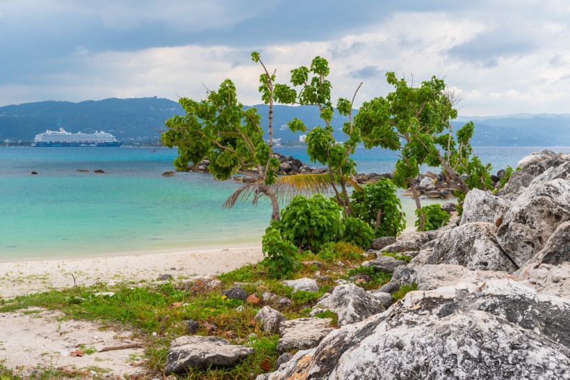 Kreuzfahrtschiff von Mein Schiff vor karibischer Küste mit Strand, Felsen und tropischer Vegetation