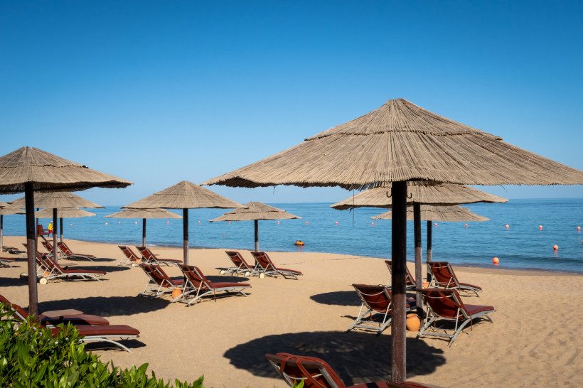Fujairah, UAE Strand mit Sonnenliegen und Strohdächern vor ruhigem, blauem Meer unter klarem Himmel
