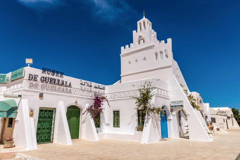 Das Musée de Guellala auf Djerba in Tunesien. Das strahlend weiße Gebäude mit grünen und blauen Türen ist mit traditionellen Ornamenten verziert und von Bougainvillea geschmückt. Ein blauer Himmel bildet den perfekten Hintergrund.