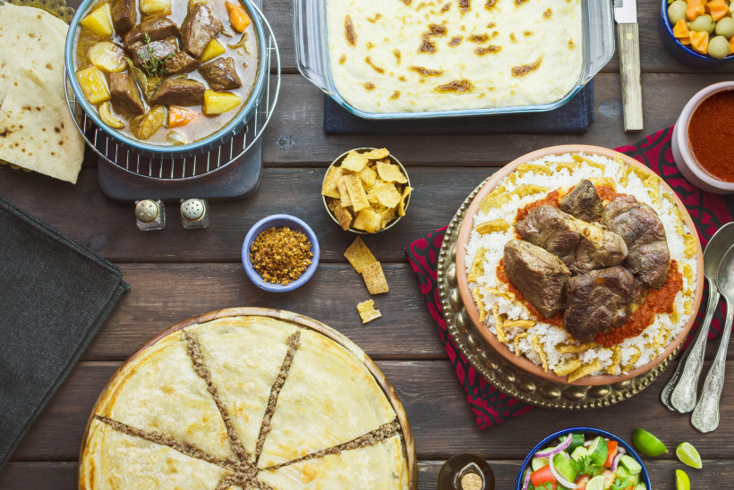 Ägypten Reich gedeckter Holztisch mit verschiedenen traditionellen Gerichten wie geschmortem Fleisch mit Reis, Fladenbrot, Eintopf mit Gemüse, gebackener Teigkuchen mit Füllung und Beilagen wie Salat, Oliven, Croutons und Saucen.
