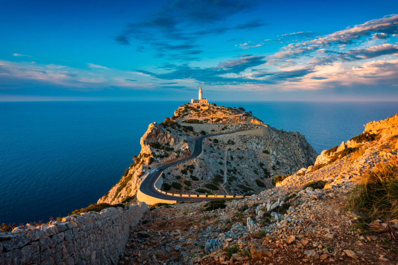 Leuchtturm am Cap de Formentor auf Mallorca über einer Felsküste, kurvenreiche Straße zum Kap und Meer im Hintergrund