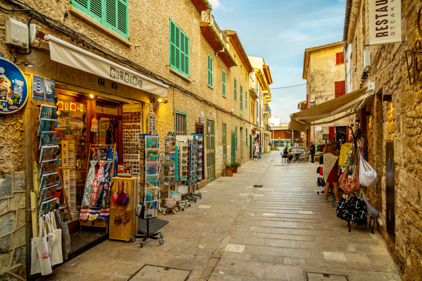 Gasse in der Altstadt von Alcúdia mit Steinhäusern, Fensterläden und Souvenirgeschäft
