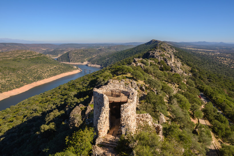 Blick über den Nationalpark Monfragüe mit Flusslauf, Brücke und Felsrücken; im Vordergrund steinerner Aussichtsturm auf einem Hügel